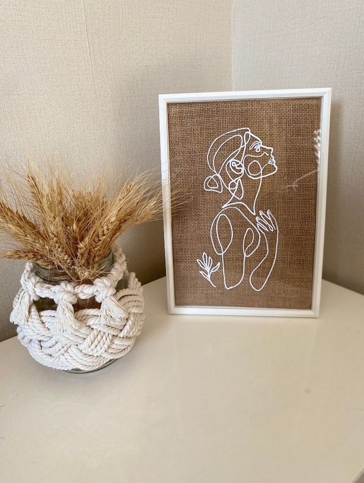 a white vase sitting on top of a table next to a framed art print with a woman's face