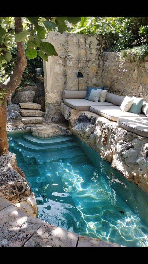 an outdoor swimming pool surrounded by stone walls and water features, including a lounge area