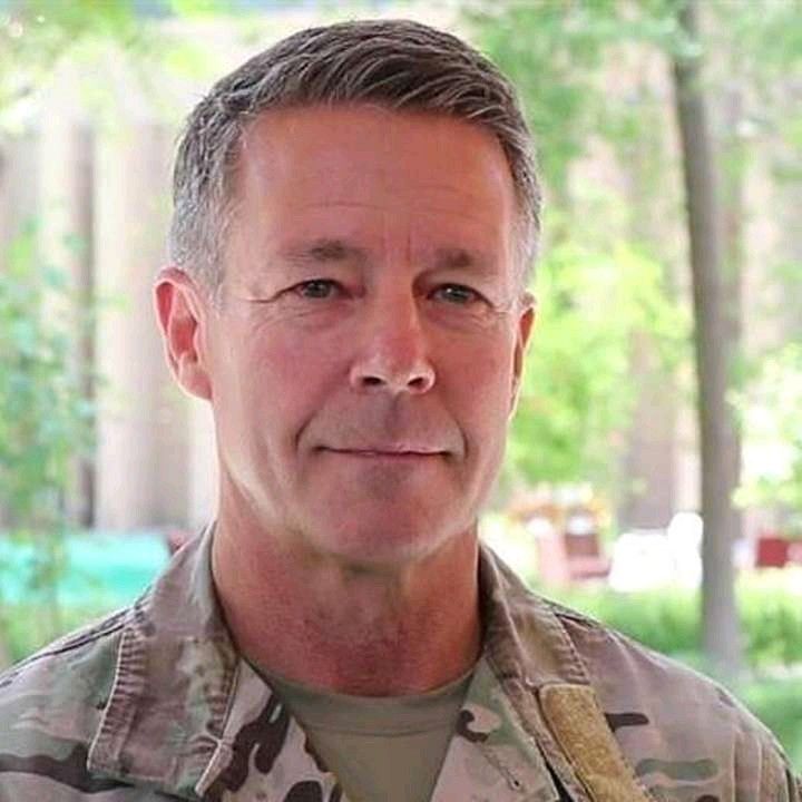 a close up of a person wearing a uniform and smiling at the camera with trees in the background