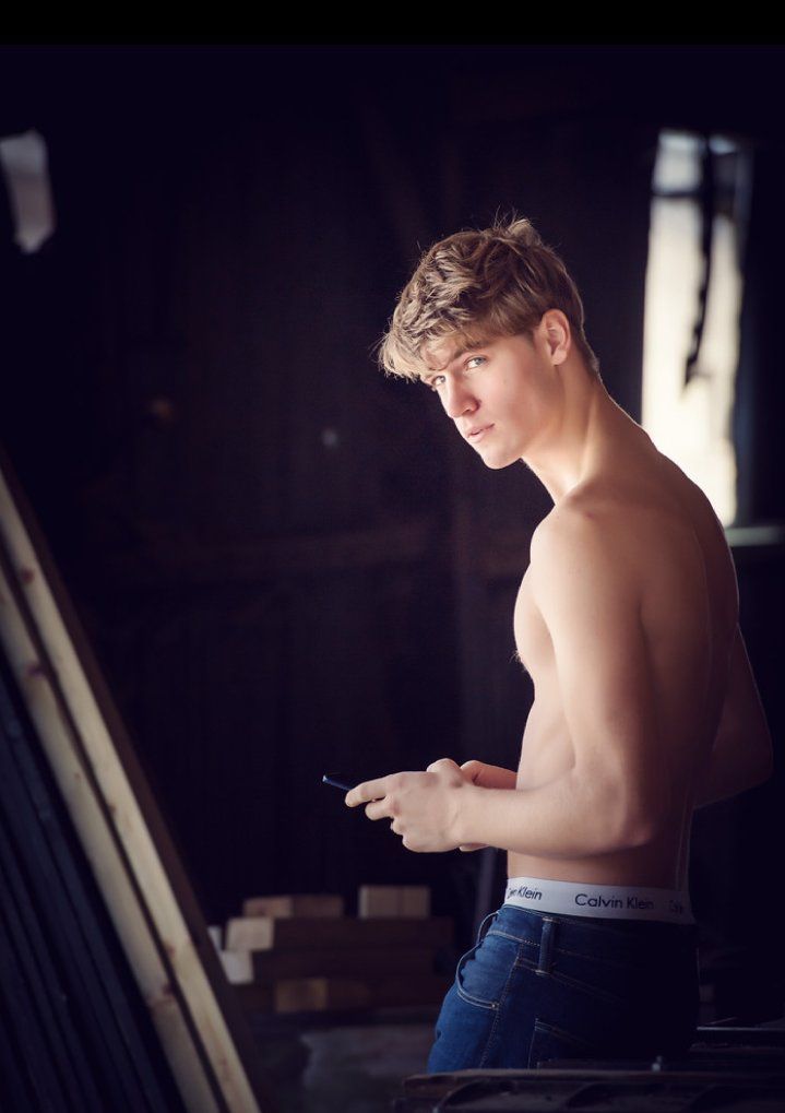 a shirtless young man holding a cell phone in his hand and looking at it