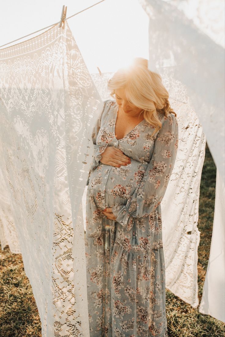 a pregnant woman is standing in front of some clothes hanging on a line and looking down at her stomach