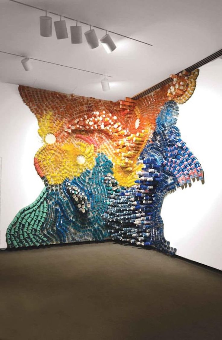 a large colorful artwork on the side of a wall in an art gallery with lights hanging from the ceiling