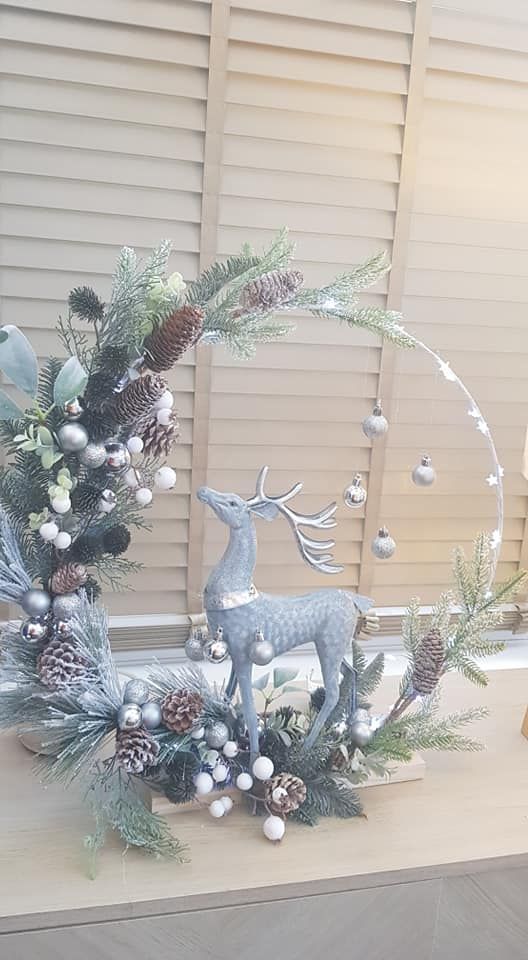 a christmas wreath with a deer, pine cones and berries in the center is displayed on a window sill