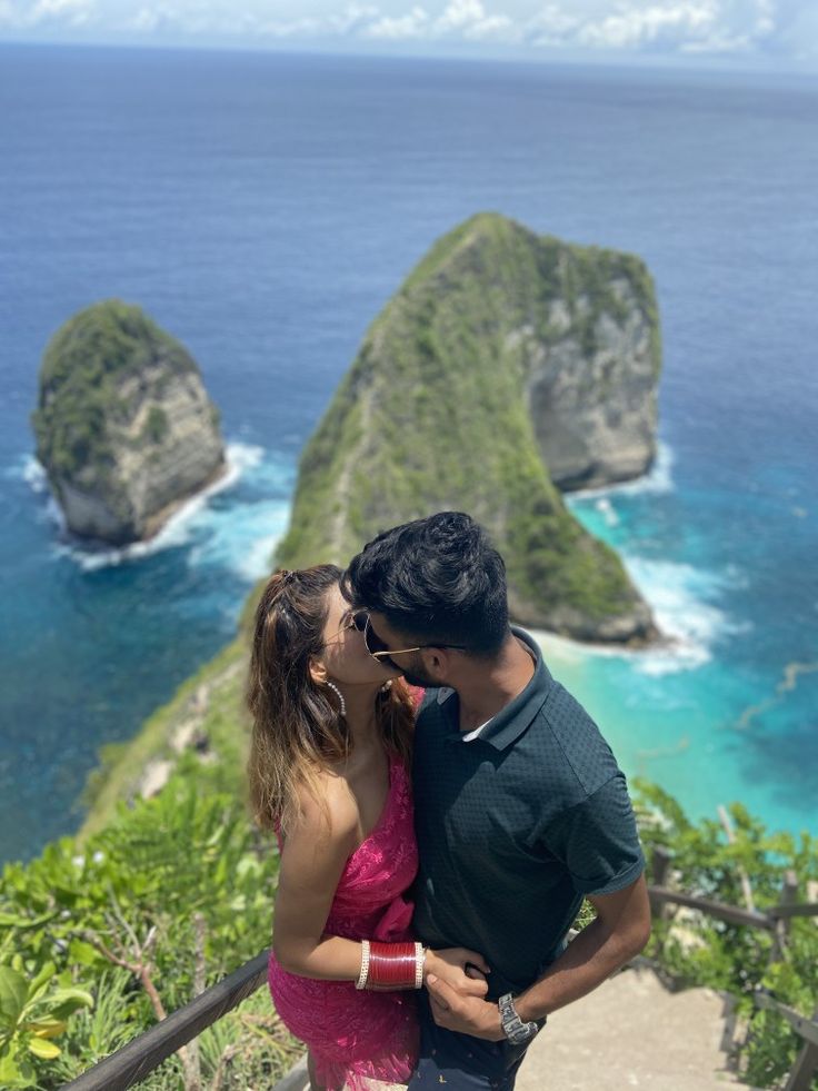 a man and woman kissing on top of a hill next to the ocean with an island in the background