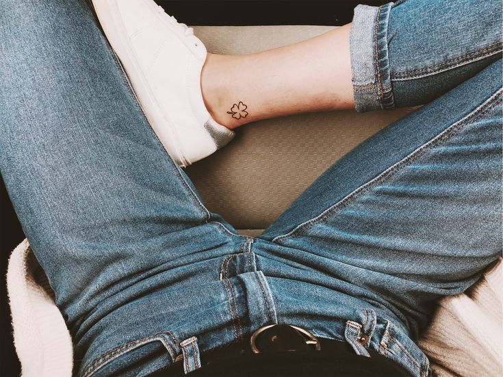 a person with a small flower tattoo on their left arm sitting in a chair and wearing blue jeans