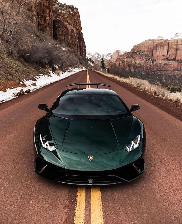 a green sports car is parked on the side of the road in front of mountains