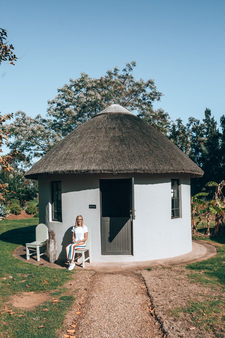 a woman sitting on a chair in front of a white building with a thatched roof