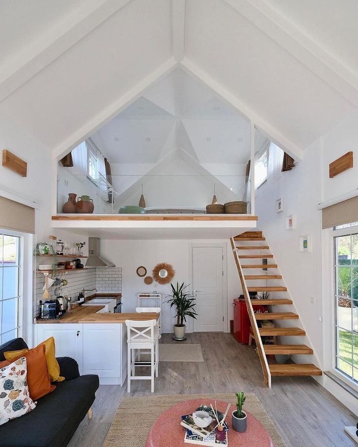 a living room filled with furniture and a stair case next to a kitchen area on top of a hard wood floor