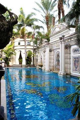 an outdoor swimming pool surrounded by palm trees and other greenery in front of a white building