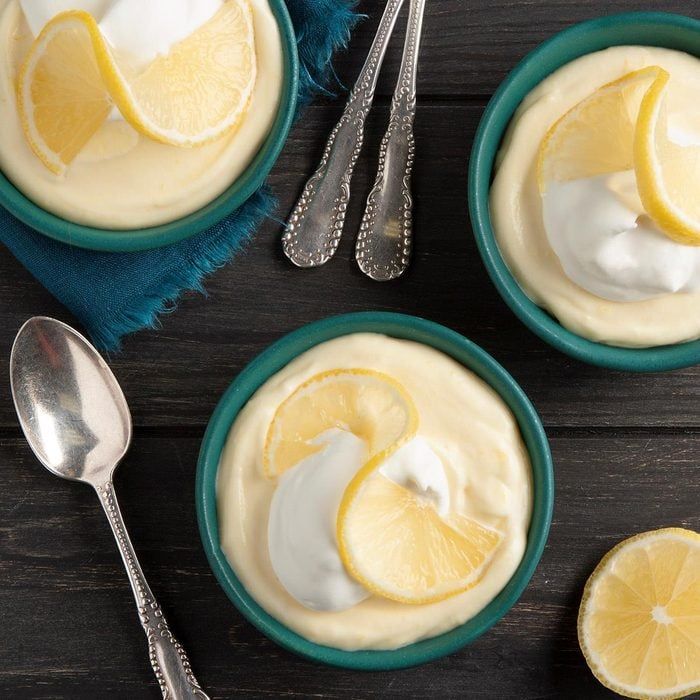 three small bowls filled with lemon custard and topped with whipped cream next to two silver spoons