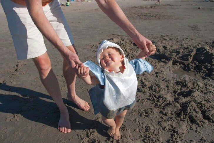 a woman holding the hand of a baby who is standing in the sand