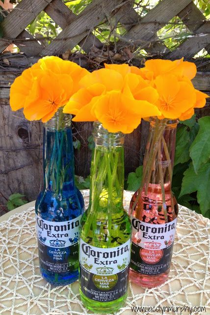 three bottles with flowers in them are sitting on a table next to some plants and a fence