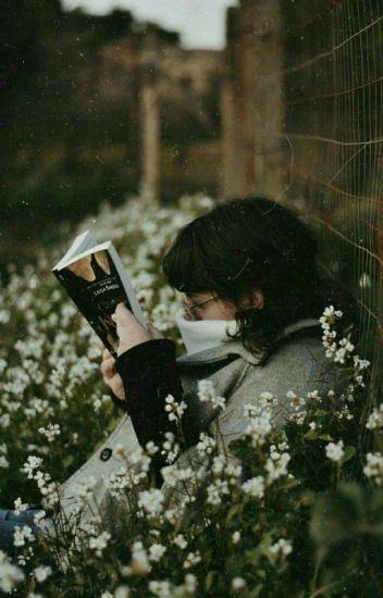 a woman sitting in the grass reading a book with white flowers around her and an old building in the background