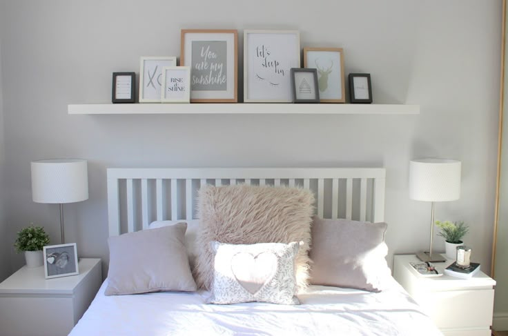 a white bed topped with pillows next to two framed pictures on top of the headboard