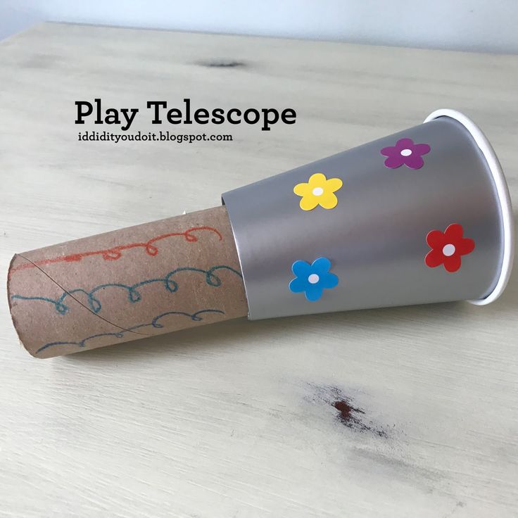 a paper tube with flowers painted on it sitting on a table next to a cup