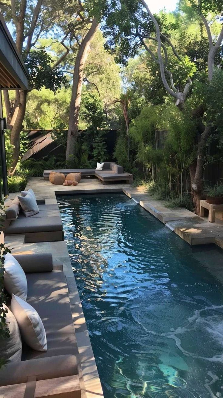 an outdoor swimming pool with lounge chairs and trees in the backround, surrounded by greenery