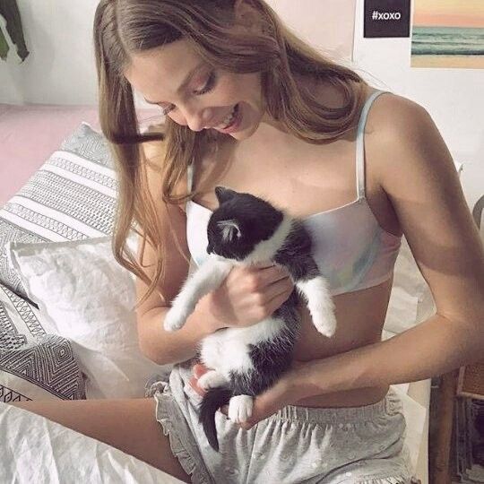 a woman holding a black and white cat in her hands while sitting on a bed