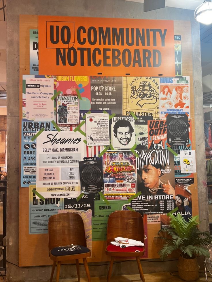 two wooden chairs sitting next to each other in front of a wall covered with posters