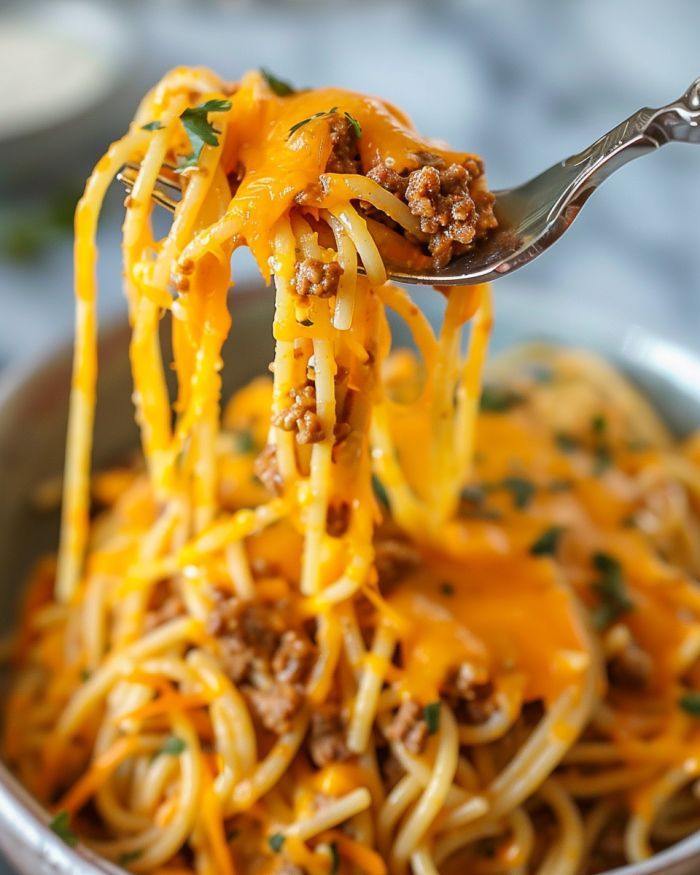 a fork full of spaghetti with ground beef and cheese on it, being lifted from a bowl