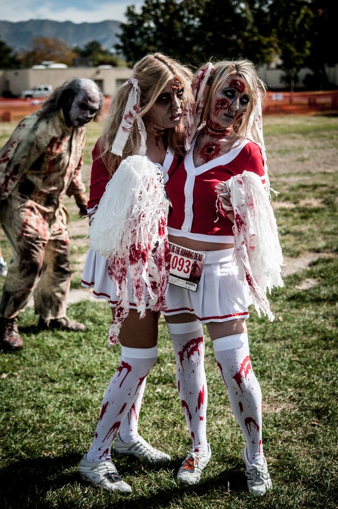 two women dressed in zombie costumes standing next to each other on the grass with zombies behind them