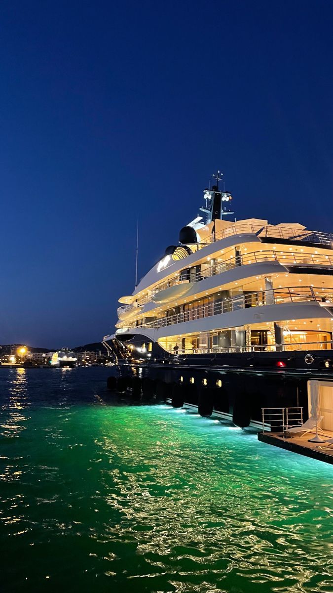 a cruise ship docked at night with lights on the deck and in the water next to it