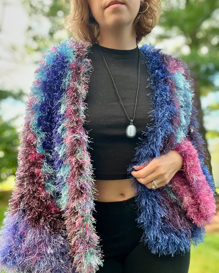 a woman with curly hair wearing a colorful jacket and black top standing in front of trees