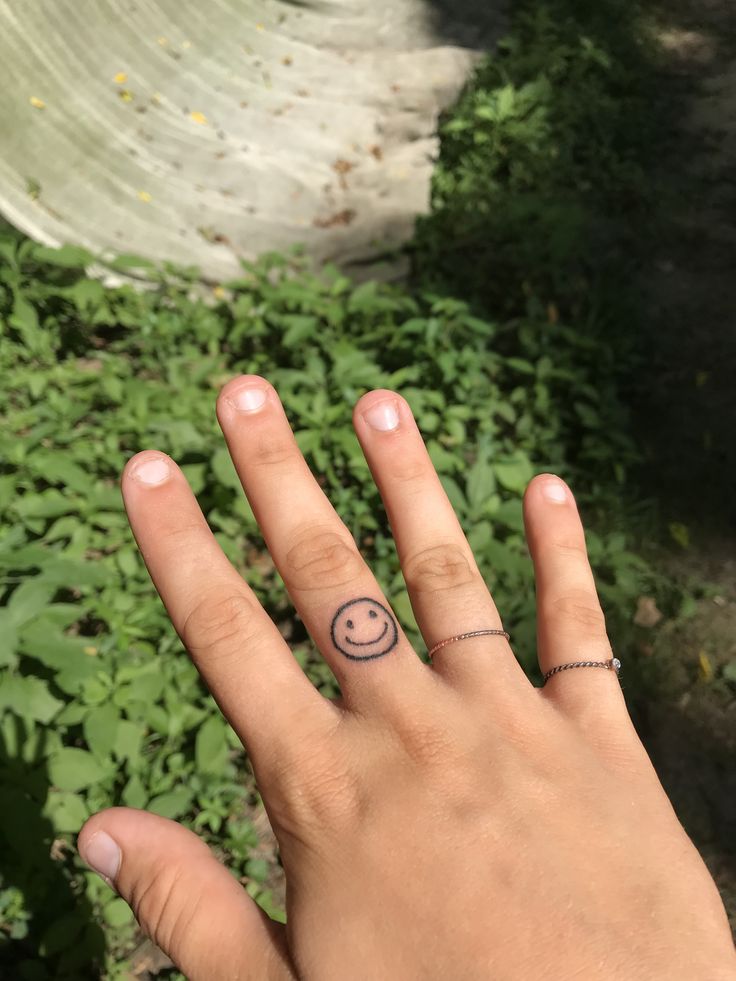 a person's hand with a small smiley face tattoo on their left ring finger