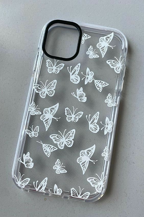 an iphone case with white butterflies on it sitting on top of a table next to a cup