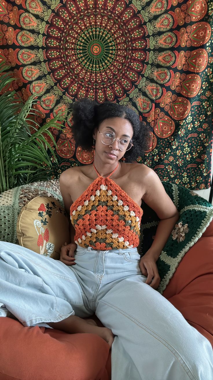 a woman sitting on top of a bed in front of a tapestry