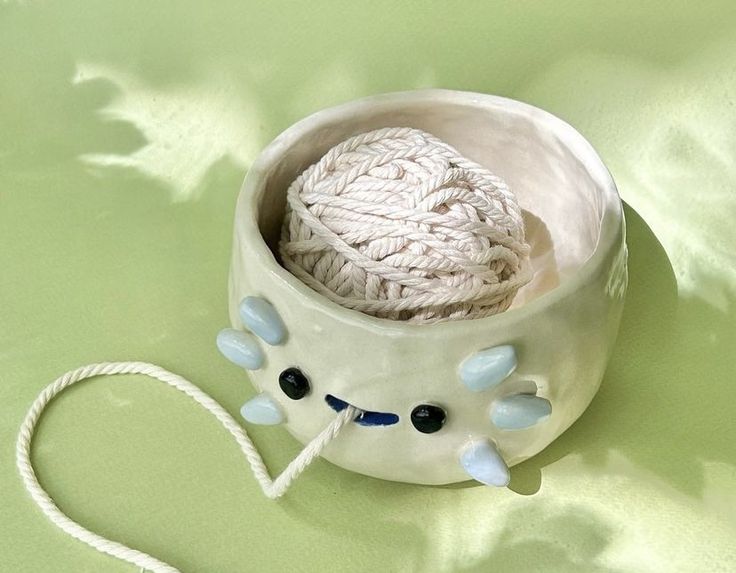 a white bowl with yarn in it sitting on a green surface