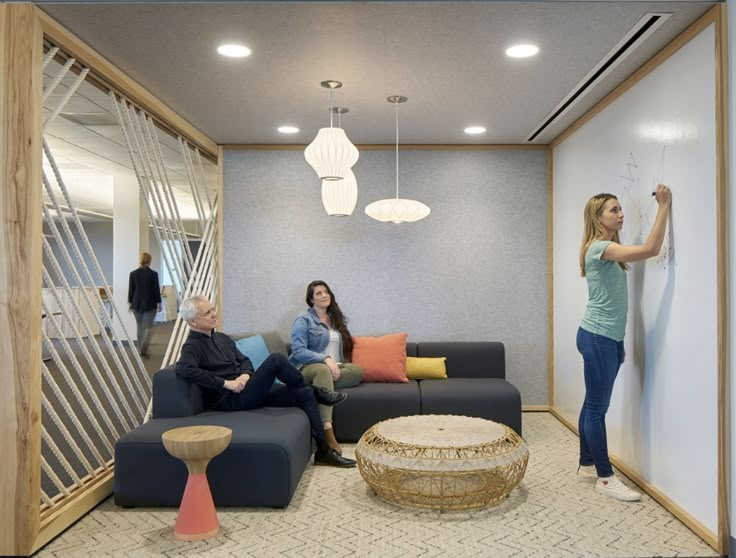 three people are sitting on couches in an office with white walls and wood trimming