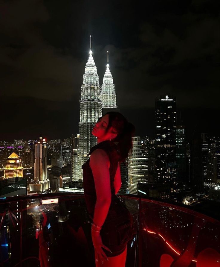 a woman standing on top of a tall building next to a city at night time