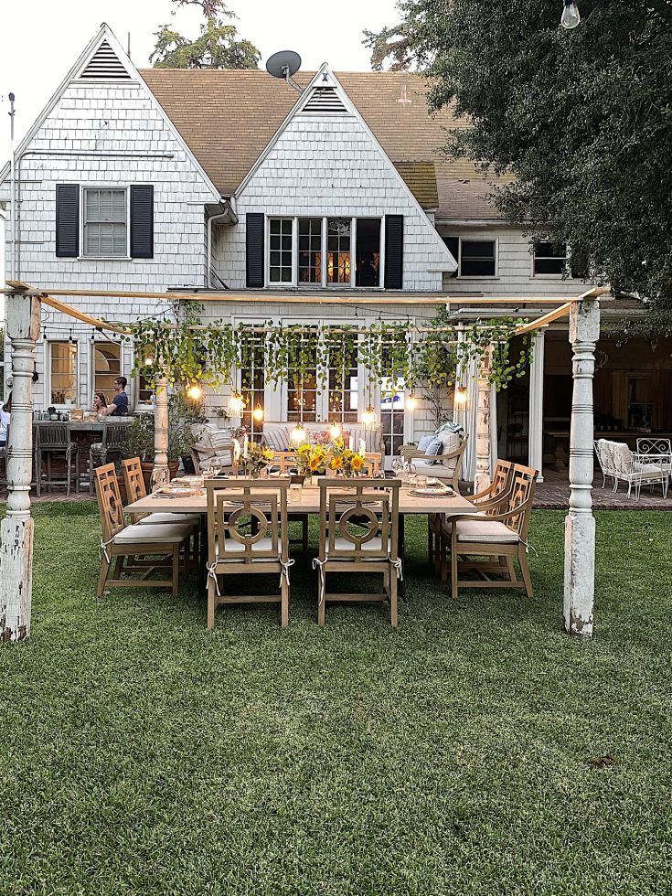 an outdoor dining table and chairs in front of a large white house with lots of windows