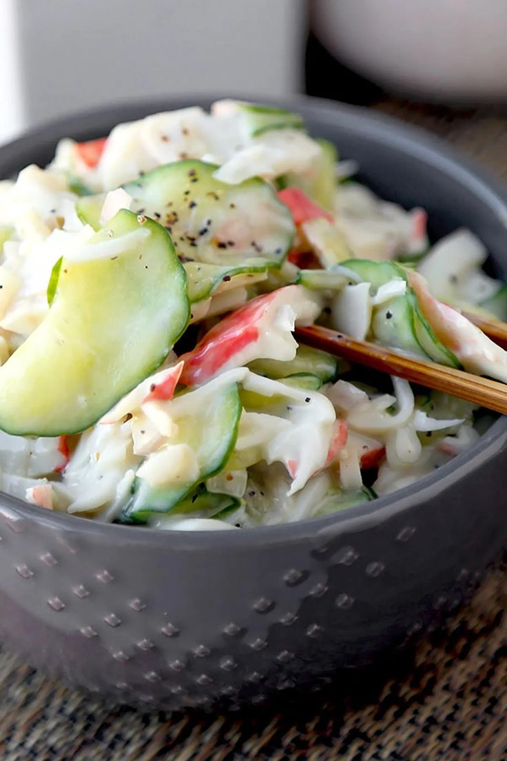 a bowl filled with cucumber and noodles next to chopsticks on a table