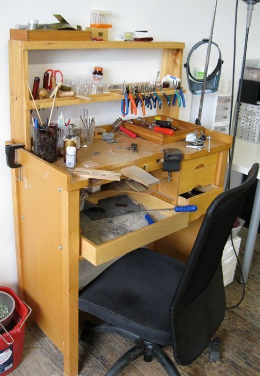 a wooden desk topped with lots of clutter and crafting supplies next to a black chair