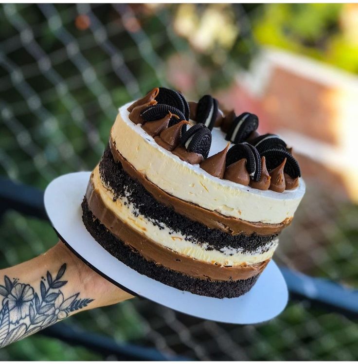 a hand holding a cake on top of a white plate with chocolate frosting and oreo cookies