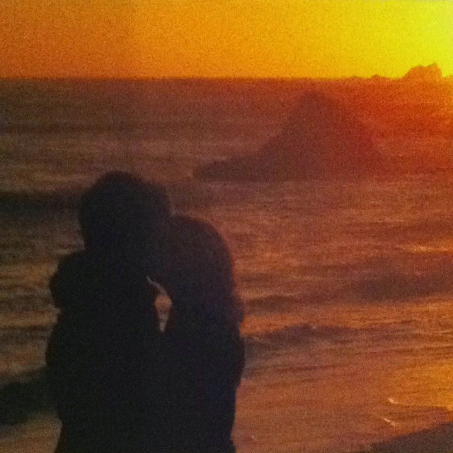 two people are kissing on the beach at sunset