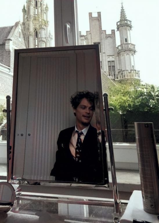 a man wearing a suit and tie in front of a mirror with an image of him