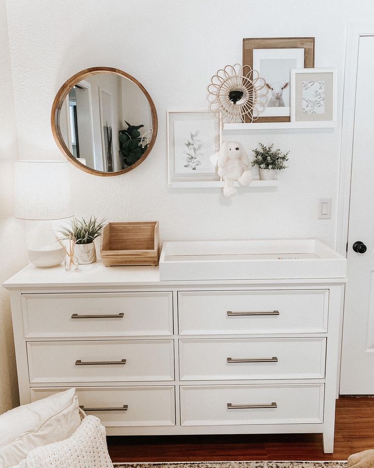 a white dresser with pictures on the wall and a mirror above it in a room