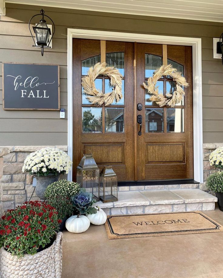 a front door with two wreaths and flowers on the steps next to an entryway