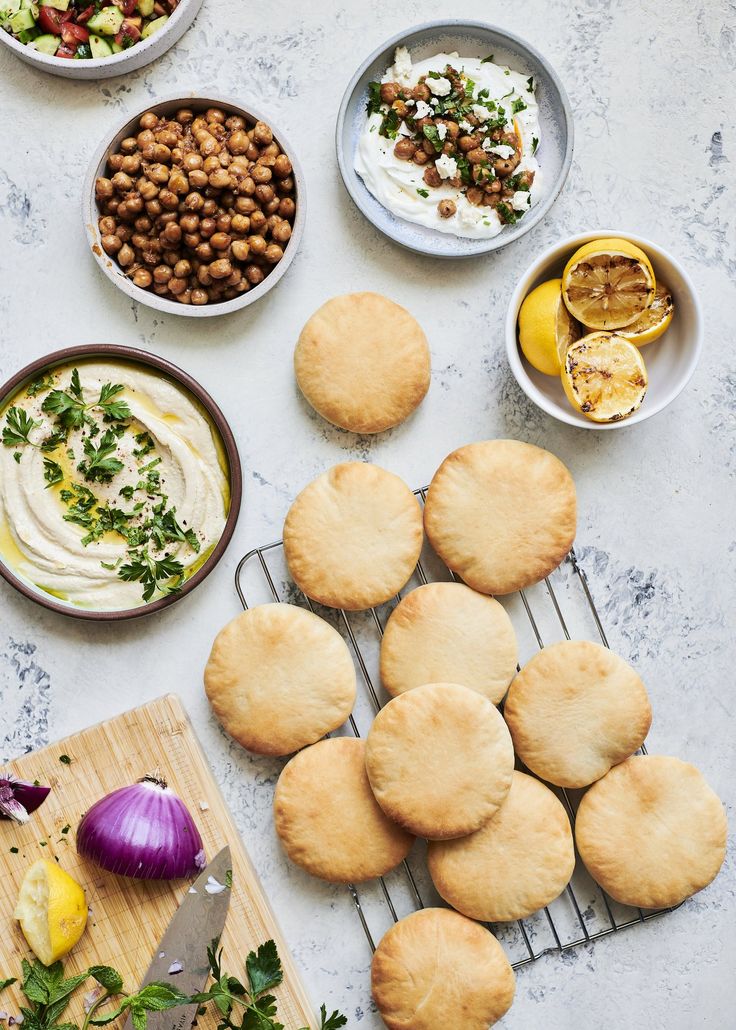 an assortment of food is laid out on a table with bread, dips and vegetables