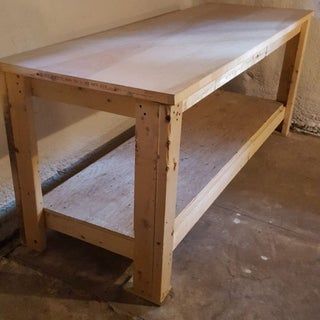 a wooden table sitting on top of a floor next to a white wall and cement floor