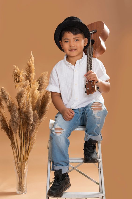 a young boy is sitting on a chair with a guitar in his hand and some dried grass behind him