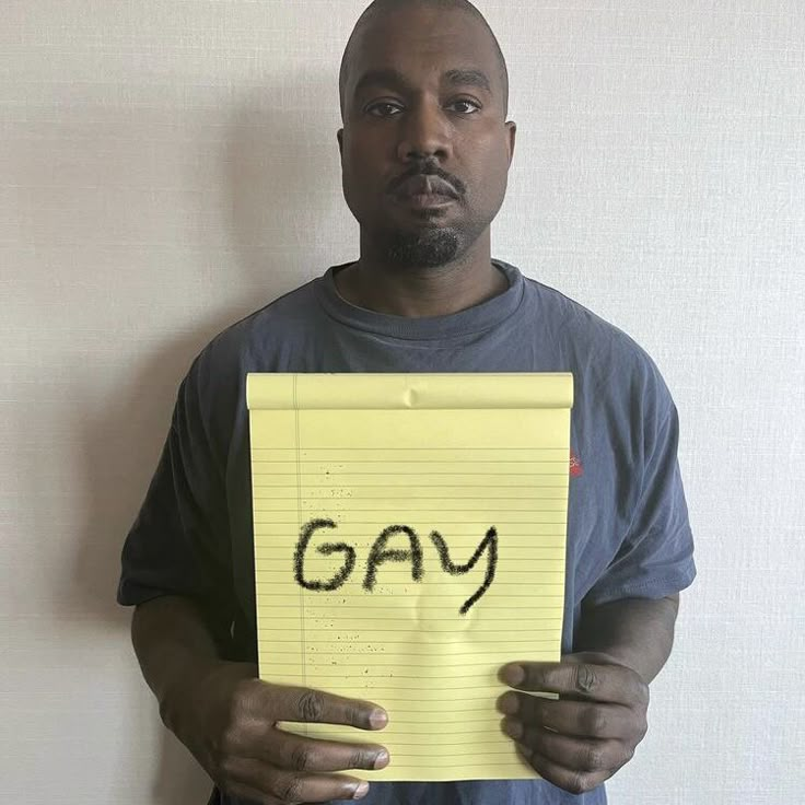 a man holding a piece of yellow paper with the word gay written on it in front of his face