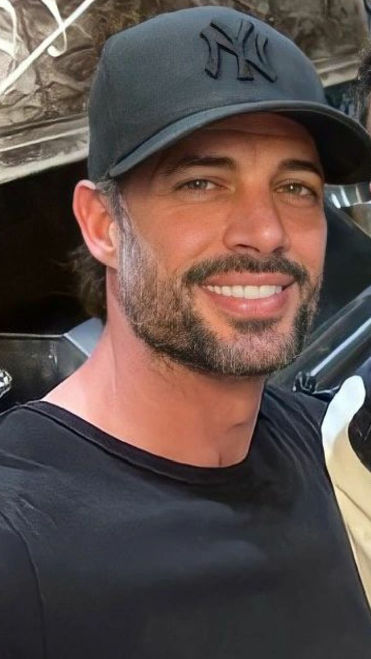 a man wearing a new york yankees hat and black t - shirt smiles at the camera