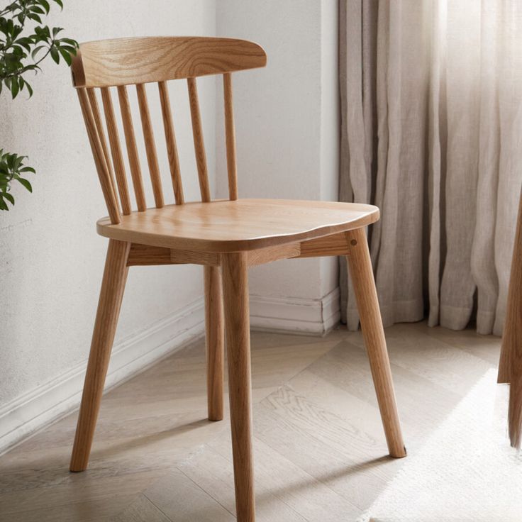 a wooden chair sitting in front of a window next to a green potted plant