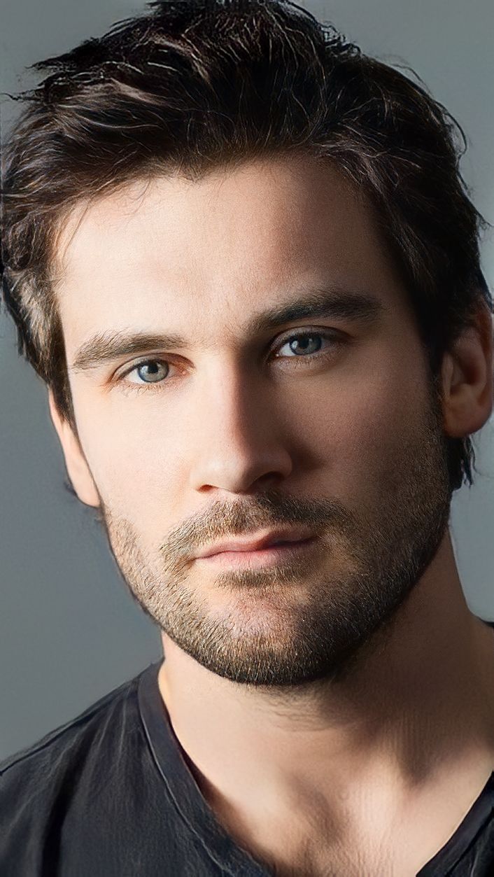 a close up of a person with a beard and blue eyes wearing a black shirt