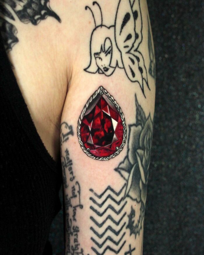 a woman's arm with tattoos on it and a red stone in the middle