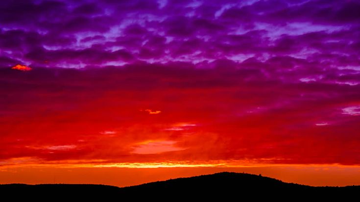 the sky is purple and red as the sun sets in the distance with mountains in the background