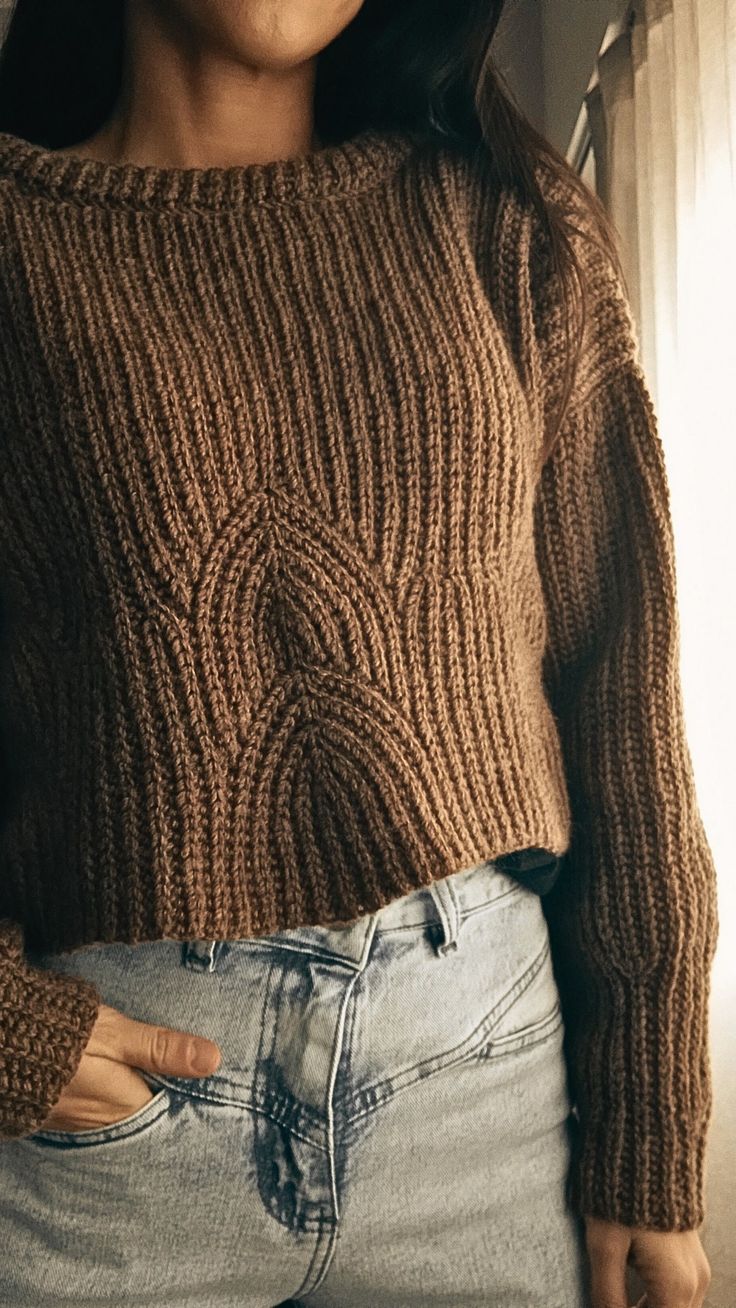 a woman is wearing a brown sweater and blue jeans with her hands in her pockets